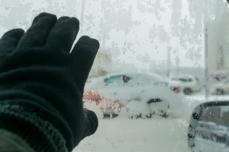 human hand on the icy glass of the car with snow patterns
