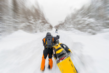 a man, an athlete in a warm sports suit rides a snowmobile on a snow-covered road