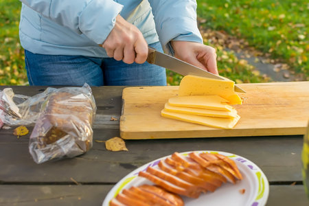 Woman with a knife cuts cheese on a wooden tableの写真素材