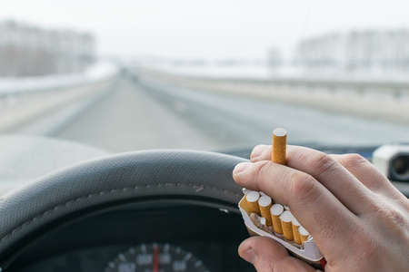 View of a car driver hand holding a pack of cigarettes while driving on the highwayの写真素材