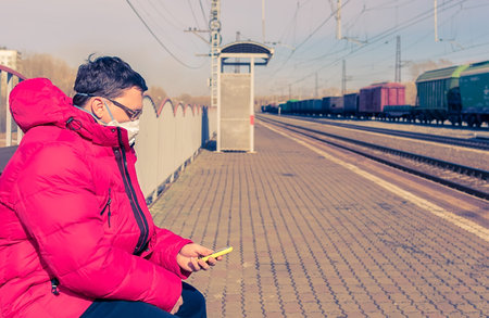 man in an antiviral medical mask sits on a bench on the platform
