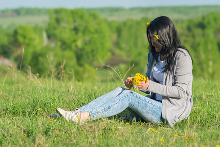 beautiful girl in a flower meadow sorting yellow dandelions