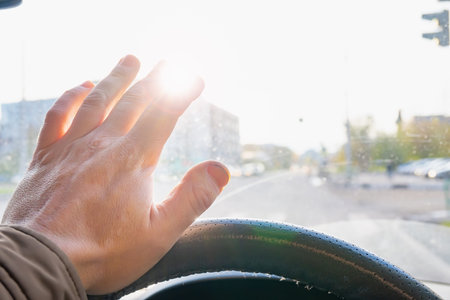 driver's hand at the wheel of the car covers the blinding sun