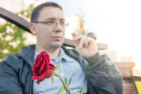 red rosebud in the hand of a thoughtful guy with glassesの写真素材