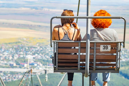 a girl with her mother, sitting on a chairlift of a cable carの写真素材