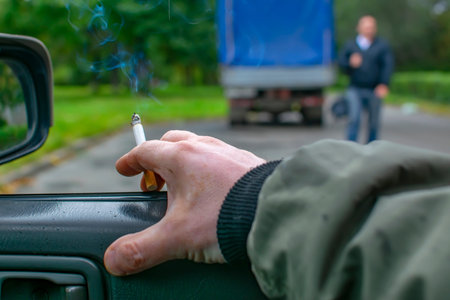 hand of a man, a driver, a smoker who is sitting in a car, holding a smoking cigaretteの写真素材