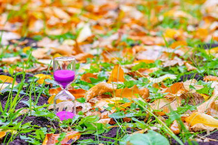 sand pours in the hourglass as a symbol, a sign of the passing time. An hourglass stands on the ground among the fallen autumn leaves before the onset of winterの写真素材