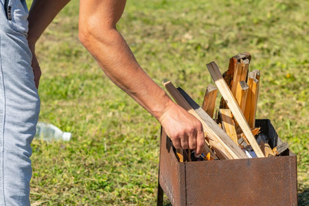 close up, a man hand lights firewood with a match in a barbecue on the streetの写真素材