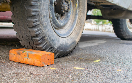 a red, orange brick lies under the wheel of an old rusty car on which the parking brake does not...