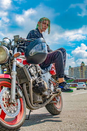a teenage guy with a hairstyle with pigtails in the form of dreadlocks is sitting on a motorcycleの写真素材