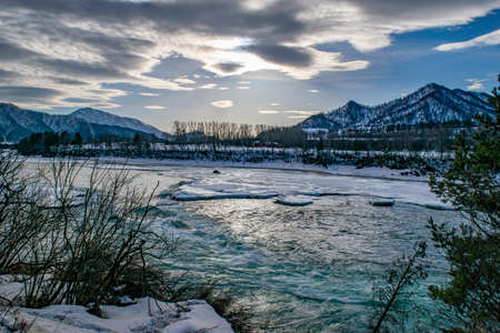 winter frosty evening gloomy landscape with a stormy river with ice and snow among the high rocky mountainsの写真素材