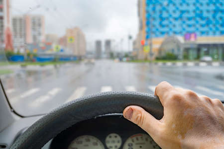the driver hand on the steering wheel inside the car against the background of the streets of an empty cityの写真素材