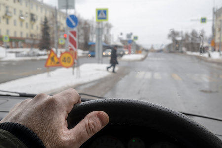driver hand behind the wheel of a car that gives way to a pedestrian at a pedestrian crossingの写真素材