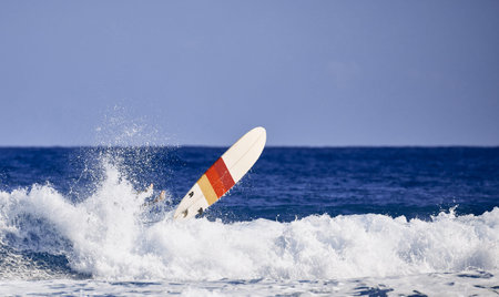 Surfer legs in water and surfing board in the air after falling a wave. Water sport activity,...