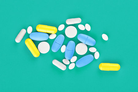 Assorted pharmaceutical medicine pills, tablets and capsules on green background.