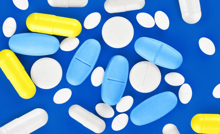Assorted pharmaceutical medicine pills, tablets and capsules on blue background.