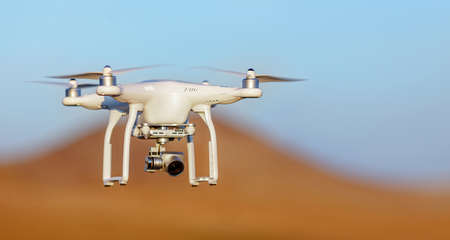 White drone quad copter with high resolution digital camera flying in the blue sky over the desert.の写真素材