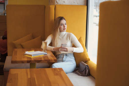 Portrait of a beautiful young blonde student girl with long hair sitting in cafe and studyingの写真素材