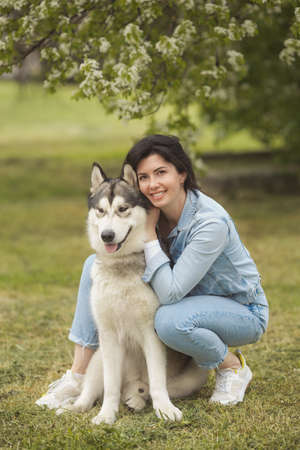 Beautiful brunette girl sitting on the grass with her funny friend malamute dogの写真素材