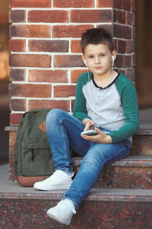 School boy listens to music on phones after school lessons or plays online gamesの写真素材