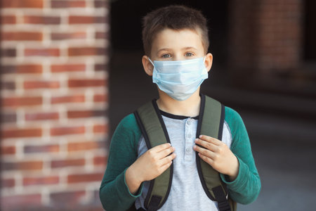 Little boy in protective mask and backpack on face goes to school. New normal.