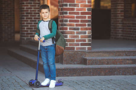 School boy in casual clothes and backpack goes to school on a scooterの写真素材