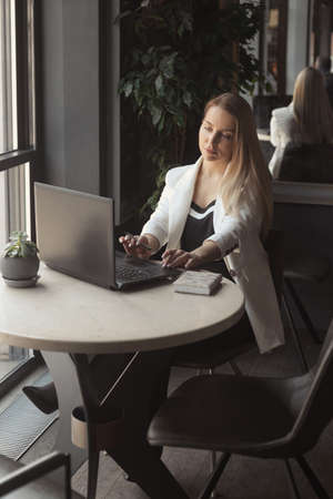 Business woman drink coffee in a white jacket and working with laptop in cafe with dark black interiorの写真素材