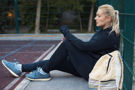 Young overweight active woman sitting on the street workout place. Tired plus-size girl in sportswear training outdoorの写真素材