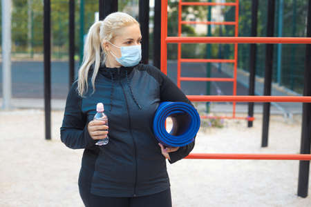 Tired blonde plus-size girl in sportswear maintains social distance,tries to lose weight with training outdoor.の写真素材