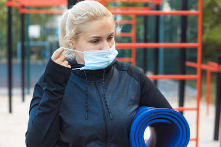 Tired blonde plus-size girl in sportswear maintains social distance,tries to lose weight with training outdoor.の写真素材