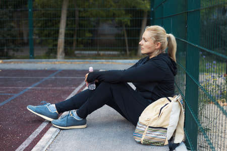 Young overweight active woman sitting on the street workout place. Tired plus-size girl in sportswear training outdoorの写真素材