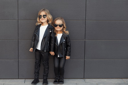 Two sisters in same outfits: white t-shirts, leather black jackets and leggings, sunglasses hearts.の写真素材