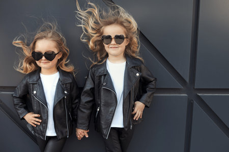 Two sisters in same outfits: white t-shirts, leather black jackets and leggings, sunglasses hearts.の写真素材