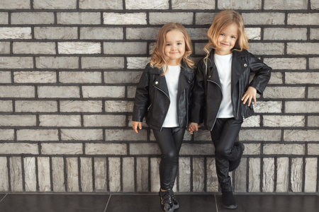 Two pretty sisters in same outfits: white t-shirts, leather black jackets and leggingsの写真素材