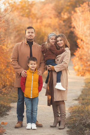 Happy family hugging on a walk in the fall park. Portrait of a caucasian mother and father holding their children in beautiful outfits on a sunny autumn day in forest. Family lifestyle concept.の写真素材