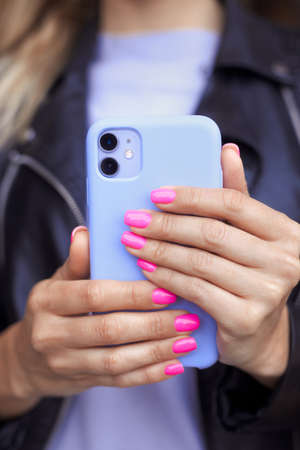 Close up vertical photo of female hands with bright neon pink manicure hold a smartphone in a purple case. No face. Young girl with fashion violet manicure taking a selfie photo on a mobile phoneの写真素材