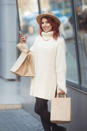 Street style portrai of happy millennial fashion woman with many craft bags after sale shopping standing next to the entrance to the shopping mallの写真素材