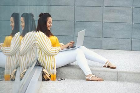 Portrait of beautiful plus size woman 30-35 years old in fashion clothes and eyeglasses working remotely on a laptop on vacation. Close-up female freelancer typing on a computer in the park outdoorsの写真素材