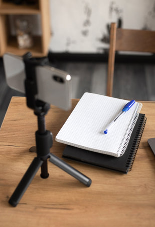 Comfortable workspace for office manager, business or freelancer in a stylish room with green plants for remote work and online video conference using a mobile phone on a tripodの写真素材