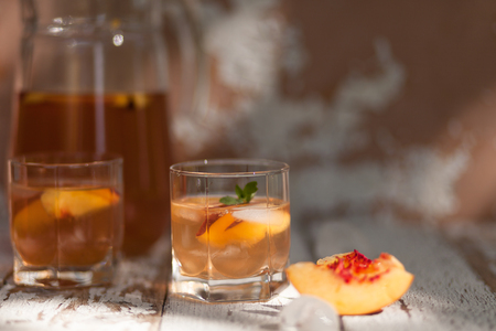 Ice tea and nectarine. Jag, two glasses.  A refreshing summer drink. The concept of summer. On a white wooden  background. Side viewの写真素材
