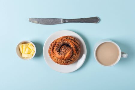 One bun with poppy seeds, butter and coffee with milk on a blue backgroundの写真素材