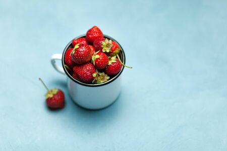 Strawberries in white enamel mug on a blue backgroundの写真素材