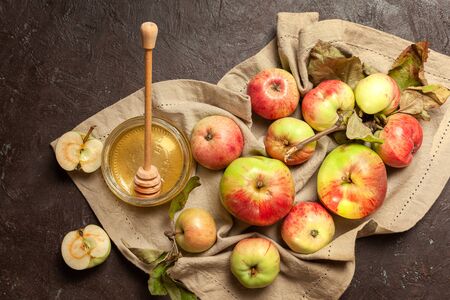 Ripe garden striped apples with leaves and a jar of honey on a beige napkin and textured background. Autumn harvestの写真素材