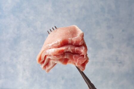 Raw pork loin on a fork. Pieces of meat impaled on a fork. On a blue background. The concept of a BBQの写真素材
