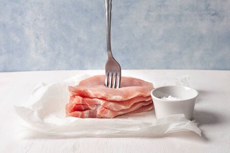 Raw pork loin on a fork. Pieces of meat impaled on a fork with spices. On parchment and blue backgroundの写真素材