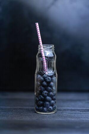 Fresh blueberries in a glass bottle on a dark wooden background. The concept of making a refreshing tea or drinkの写真素材