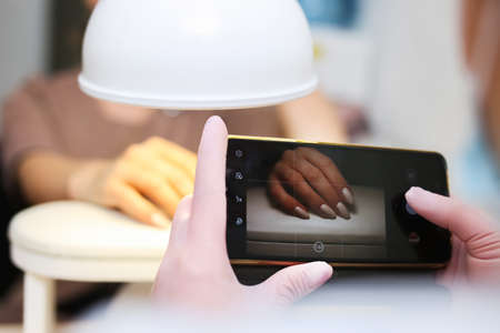 Manicurist takes a photograph of her work, beautiful woman manicure, with a smartphoneの写真素材
