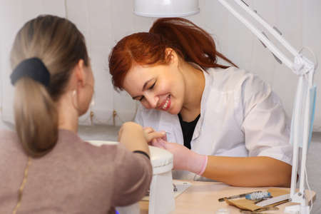 Happy smiling manicurist. Friendly warm atmosphere in the beauty salon. The process of manicure and nail care.の写真素材