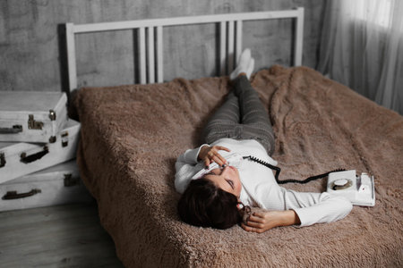 Smiling woman lying in bed and talking on the phone at home, happy young girl holding a phone,...
