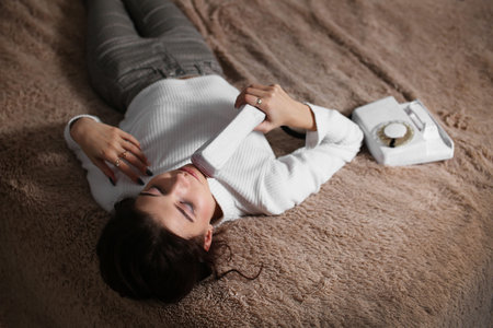 Upset young woman lying on bed next to phoneの写真素材